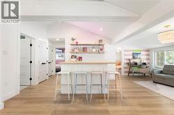 Bright interior space featuring wood-finish flooring, a built-in white bar with a light wood countertop, and white vaulted ceilings with exposed beams - 