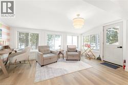 Bright interior space featuring light wood-finish flooring, multiple windows, a tiered drum chandelier, and a white paneled door with glass insert - 