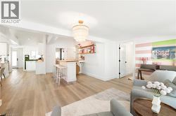 Open-concept living space with wood-finish flooring, a contemporary tiered chandelier, white shaker cabinetry, an eat-at kitchen island with a wood countertop, and built-in shelving - 