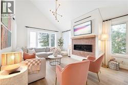 Vaulted ceiling living room featuring wood-finish flooring, a contemporary linear fireplace with a brick surround, and large windows - 