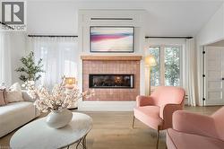 Living area featuring a tiled fireplace with wood mantel, built-in media cabinet, large windows with white sheer curtains, and light wood-finish flooring - 