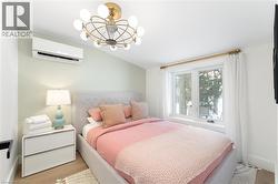 Bright room featuring light wood-finish flooring, a wall-mounted air conditioning unit, and a contemporary ceiling light fixture - 
