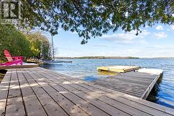 Expansive wood dock with a floating platform and a boat moored at the shoreline, all set against a clear blue lake with a distant treeline - 