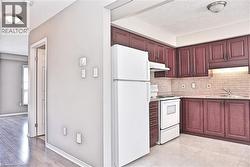 Kitchen featuring rich wood-finish cabinetry, light-toned tile backsplash, and light-toned tile flooring - 