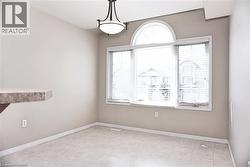 Dining area featuring an arched window, a wall-mounted light fixture, light neutral wall paint, tile flooring, and a partial breakfast bar with a stone-finish countertop - 