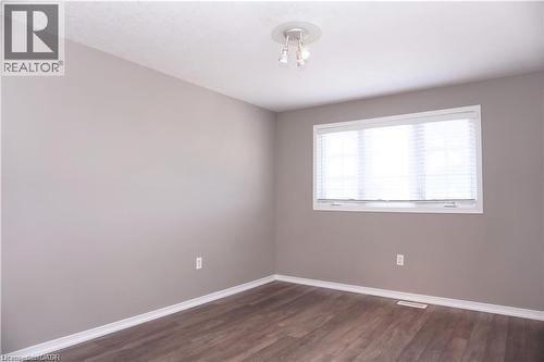 Room featuring wood-finish flooring, a window with horizontal blinds, and a flush-mount ceiling light fixture - 40 Madeleine Street, Kitchener, ON 
