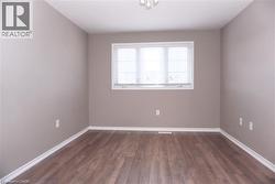 Room featuring a large window with white blinds, wood-finish flooring, and light neutral wall paint - 