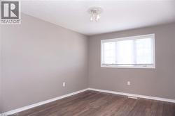 Room featuring wood-finish flooring, a window with horizontal blinds, and a flush-mount ceiling light fixture - 