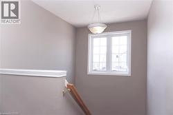 Wall-mounted staircase handrail with natural wood-tone finish, featuring a double-paned window with white trim, a semi-flush mount ceiling light fixture, and neutral-toned wall paint - 