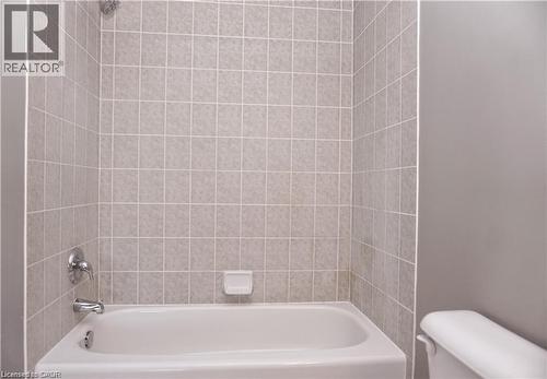 White bathtub with chrome fixtures, surrounded by light-toned square wall tiles - 40 Madeleine Street, Kitchener, ON 