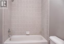 White bathtub with chrome fixtures, surrounded by light-toned square wall tiles - 