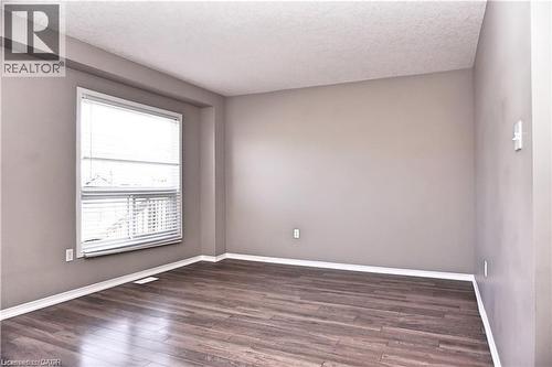 Spacious room featuring wood-finish flooring, neutral-toned walls, a large window with horizontal blinds, white baseboards, and a textured ceiling - 40 Madeleine Street, Kitchener, ON - Indoor Photo Showing Other Room