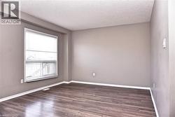 Spacious room featuring wood-finish flooring, neutral-toned walls, a large window with horizontal blinds, white baseboards, and a textured ceiling - 