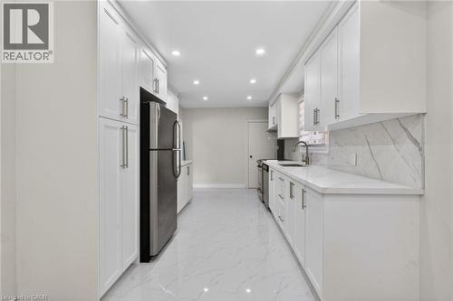 Galley kitchen featuring extensive white cabinetry with brushed nickel hardware, a stainless steel refrigerator, and a matching range - 53 Nicklin Crescent, Guelph, ON - Indoor Photo Showing Kitchen