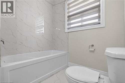 Bathroom featuring a white soaking tub with polished chrome fixtures, white marbled tile surround, and a white toilet - 53 Nicklin Crescent, Guelph, ON - Indoor Photo Showing Bathroom