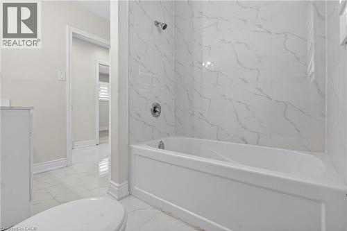 Bathroom featuring a white porcelain bathtub with chrome fixtures, surrounded by large format white tiles with subtle grey veining - 53 Nicklin Crescent, Guelph, ON - Indoor Photo Showing Bathroom