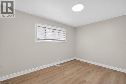 Neutral-toned room featuring a single window with horizontal blinds, wood-finish flooring, white baseboards, and a circular flush-mount ceiling light fixture - 53 Nicklin Crescent, Guelph, ON - Indoor Photo Showing Other Room