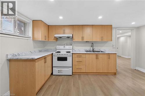 Kitchen featuring L-shaped wood-finish cabinetry with brushed nickel hardware, light-toned countertops, a white electric range, and a stainless steel sink with a high-arc faucet - 53 Nicklin Crescent, Guelph, ON - Indoor Photo Showing Kitchen With Double Sink