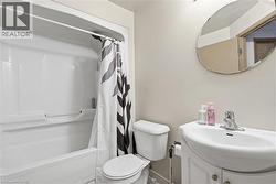 Bathroom featuring a white bathtub with a shower, a toilet, a vanity with an integrated sink, and an oval mirror - 