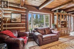 Living area featuring a bay window, exposed log walls, a beamed ceiling, and wood-finish flooring - 