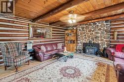 Living area featuring log walls, wood-finish ceiling, exposed log beams, a prominent stone fireplace, and a built-in wood shelving unit - 