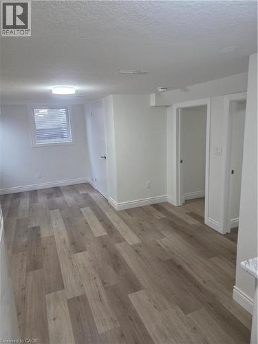 Spacious room featuring wood-finish flooring, white baseboards, and a large egress window - 22 Montrose Avenue, Kitchener, ON - Indoor Photo Showing Other Room