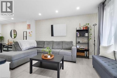Bright living area featuring wood-finish flooring, recessed lighting, a window with sheer and blackout curtains, and patterned wall accents - 133 Frederick Avenue, Hamilton, ON - Indoor Photo Showing Living Room