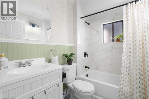 Bathroom featuring a white vanity with integrated sink, beadboard wainscoting, and a bathtub with white marble-look tile surround - 133 Frederick Avenue, Hamilton, ON - Indoor Photo Showing Bathroom