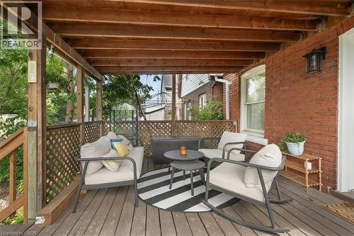 Wood-finish covered deck featuring a lattice railing, natural wood ceiling beams, and a brick exterior wall with a wall-mounted light fixture - 133 Frederick Avenue, Hamilton, ON - Outdoor With Deck Patio Veranda With Exterior