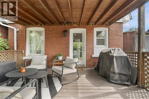 Covered rear deck featuring wood plank flooring, exposed wood beam ceiling, brick exterior, lattice railing, and exterior wall-mounted lighting - 133 Frederick Avenue, Hamilton, ON - Outdoor With Deck Patio Veranda With Exterior