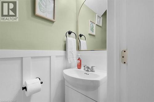 Pedestal sink with chrome faucet, board and batten wainscoting, arched mirror, and sage green walls - 133 Frederick Avenue, Hamilton, ON - Indoor Photo Showing Bathroom