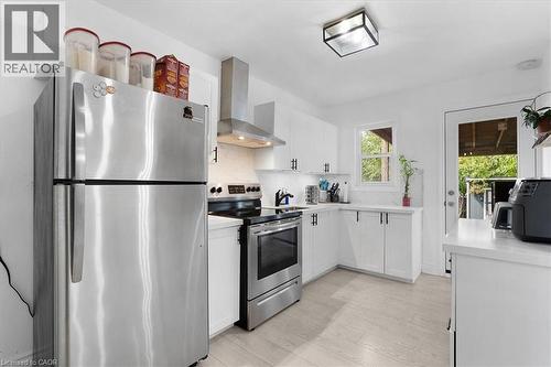 Kitchen featuring stainless steel appliances, white cabinetry with dark hardware, a corner window, and light wood-finish flooring - 133 Frederick Avenue, Hamilton, ON - Indoor Photo Showing Kitchen