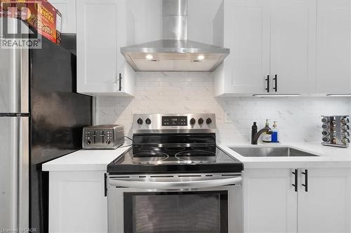 Modern kitchen featuring white shaker cabinetry, stainless steel appliances, white subway tile backsplash, white countertops, and a stainless steel sink with a dark-finish faucet - 133 Frederick Avenue, Hamilton, ON - Indoor Photo Showing Kitchen
