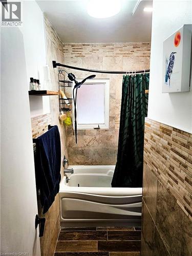 Bathroom featuring a white tub with a curved apron, stone-look wall tiles, a mosaic tile accent band, a frosted window, and wood-finish floor tiles - 34 Christopher Drive, Cambridge, ON - Indoor Photo Showing Other Room