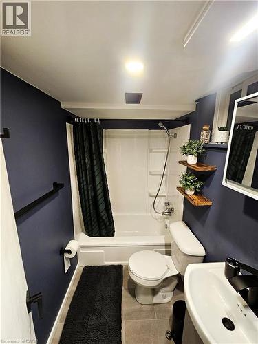 Bathroom featuring a white tub/shower combination, dark walls, matte black fixtures, a wall-mounted mirror, and wood-finish floating shelves - 34 Christopher Drive, Cambridge, ON - Indoor Photo Showing Bathroom