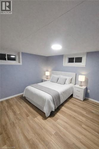 Wood-finish flooring throughout, featuring a light blue wall finish, two recessed windows with white trim, and overhead flush-mount lighting - 34 Christopher Drive, Cambridge, ON - Indoor Photo Showing Bedroom