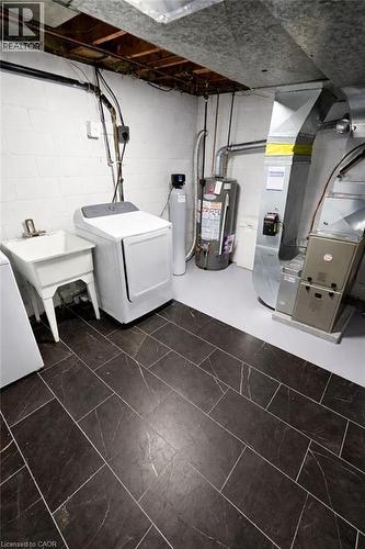 Utility area featuring dark rectangular tile flooring, white block walls, exposed ceiling joists, and a white utility sink - 34 Christopher Drive, Cambridge, ON - Indoor
