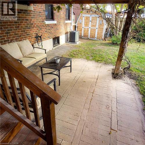 Brick exterior featuring a covered patio with stamped concrete flooring, wooden railing, and a detached storage shed - 34 Christopher Drive, Cambridge, ON - Outdoor