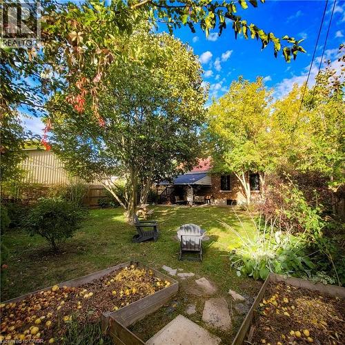 Spacious backyard featuring multiple mature trees, a manicured lawn area, two raised garden beds, and stepping stones leading to the brick exterior of the property - 34 Christopher Drive, Cambridge, ON - Outdoor