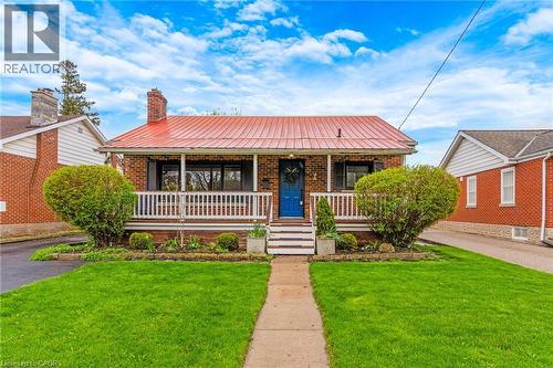 Brick exterior featuring a bright red metal roof, covered front porch, and a vibrant blue entry door - 34 Christopher Drive, Cambridge, ON - Outdoor With Deck Patio Veranda