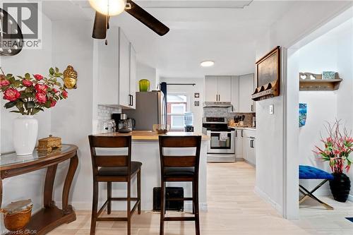 Contemporary kitchen featuring light wood-finish flooring, white cabinetry, stainless steel appliances, a subway tile backsplash, and a breakfast bar with seating - 34 Christopher Drive, Cambridge, ON - Indoor Photo Showing Other Room