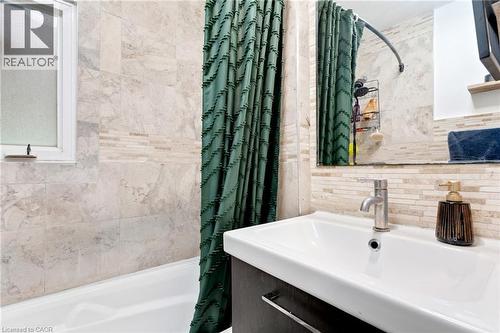 Bathroom featuring a white bathtub, frosted window, light-toned wall tiling, and a vanity with an integrated sink and chrome faucet - 34 Christopher Drive, Cambridge, ON - Indoor Photo Showing Bathroom