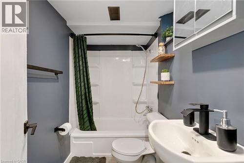 Compact bathroom featuring a white tub/shower combination, wall-mounted sink, and floating wood shelves - 34 Christopher Drive, Cambridge, ON - Indoor Photo Showing Bathroom