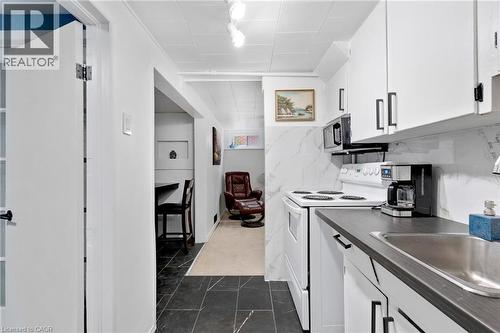 Compact kitchen featuring white cabinetry with dark hardware, dark countertops, white range, and built-in microwave - 34 Christopher Drive, Cambridge, ON - Indoor Photo Showing Kitchen