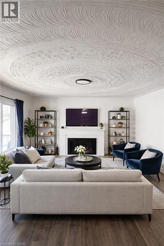 Living area featuring a textured ceiling with a central light fixture, a fireplace with a white mantel, and wood-finish flooring - 34 Christopher Drive, Cambridge, ON - Indoor Photo Showing Living Room With Fireplace