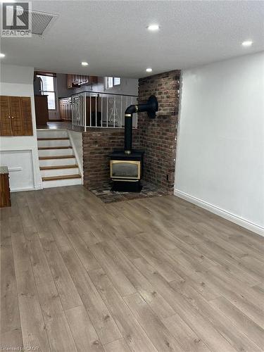 Spacious interior featuring wide plank wood-finish flooring, a brick accent wall with a wood-burning stove, recessed lighting, and a white metal staircase railing - 744 Parkview Crescent, Cambridge, ON - Indoor Photo Showing Other Room With Fireplace