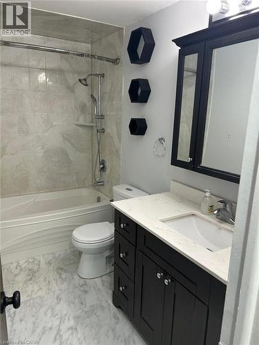 Bathroom featuring a dark wood-finish vanity with a light-toned countertop, a built-in tub with tile surround, a wall-mounted shower system, and marble-look floor tiles - 744 Parkview Crescent, Cambridge, ON - Indoor Photo Showing Bathroom