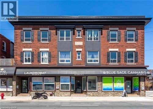 The property features a brick exterior with dark shutters on the windows, and a dark roofline - 833 King Street E, Hamilton, ON 