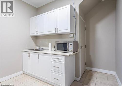 Utility space featuring white cabinetry with silver hardware, a stainless steel sink, and light-colored tiled flooring - 833 King Street E, Hamilton, ON 