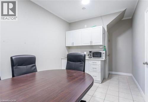 This room features a dark wood oval table, white upper and lower cabinetry, and light-toned floor tiles - 833 King Street E, Hamilton, ON 